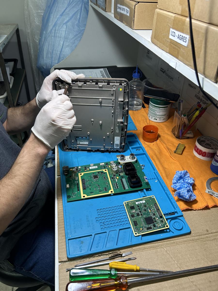 Técnico da AGROGPS abrindo um monitor agrícola na bancada do laboratório, com as placas eletrônicas expostas